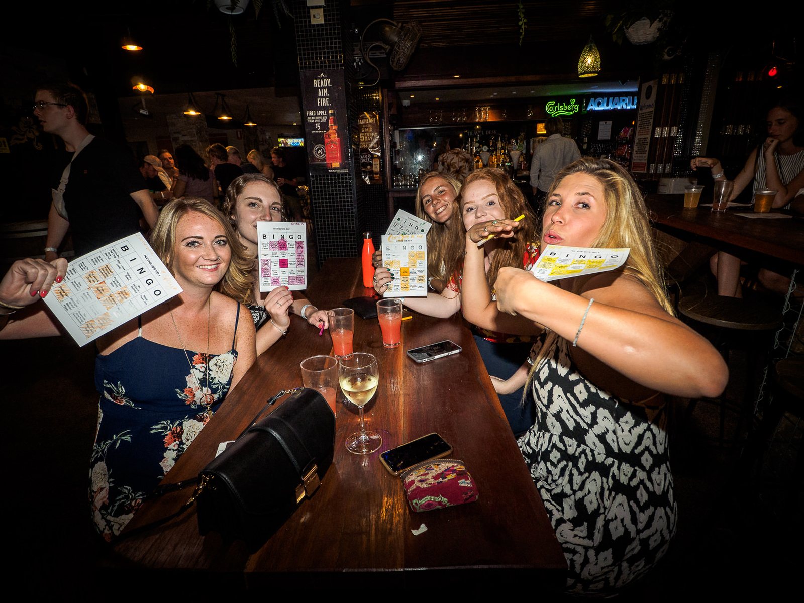 Players holding up printed Mix Tape Music Bingo cards at a bar